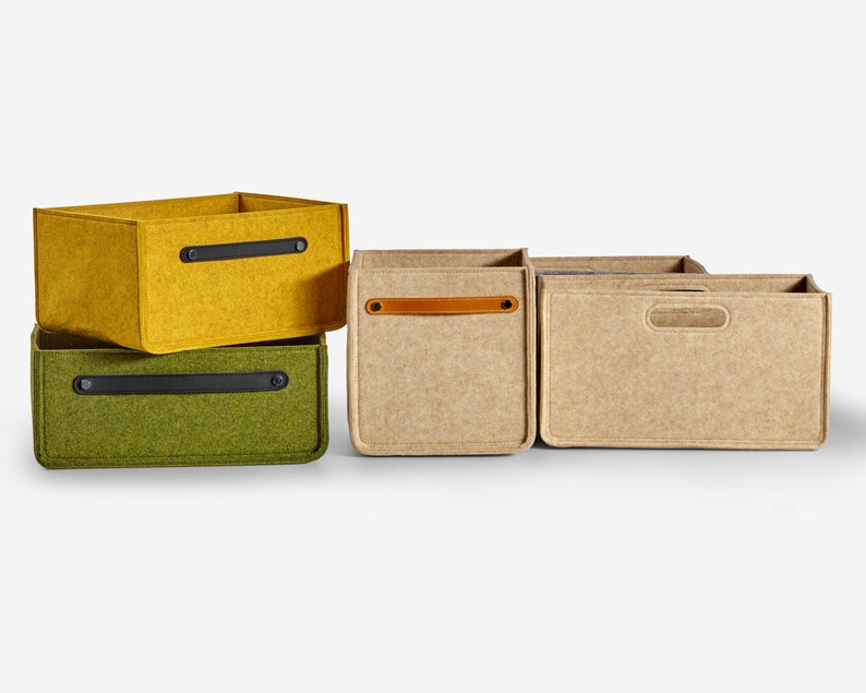 May include: Three felt storage boxes with leather handles. The boxes are stacked on top of each other. The top box is yellow, the middle box is green, and the bottom box is beige.
