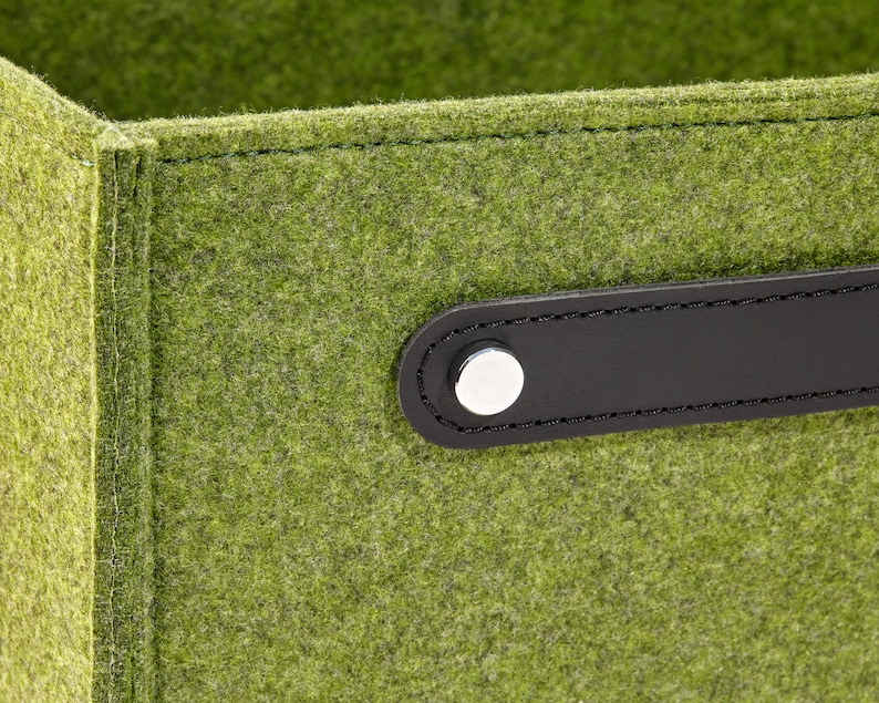 May include: A green felt storage box with a black leather handle and a silver metal button. The box is made of a soft, durable material and is perfect for organizing small items.