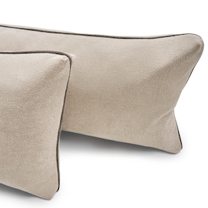 Puede incluir: Dos cojines rectangulares beige con ribete marrón oscuro. Los cojines tienen una tela texturizada y se muestran sobre un fondo blanco. Los cojines son de color neutro y complementarían una variedad de estilos de decoración del hogar.