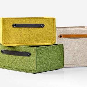 May include: Three felt storage boxes with leather handles. The top box is yellow, the middle box is green, and the bottom box is beige.