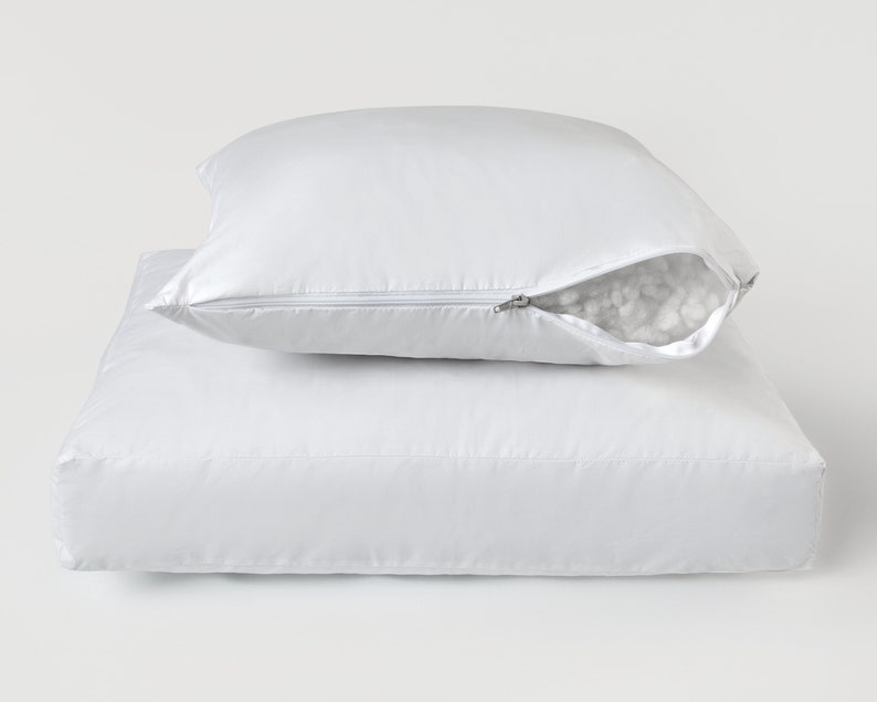 May include: A white zippered pillow with a white cotton filling. The pillow is on top of a white pillowcase.