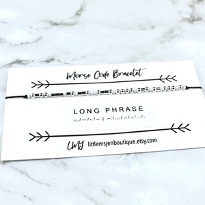 May include: A white card with black text and arrows reads "Morse Code Bracelet" and "LONG PHRASE" with a black string bracelet with white and black beads. The card also includes the text "My littlemsjenboutique.etsy.com".