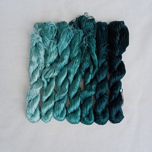 May include: Six skeins of embroidery floss in shades of green, ranging from light to dark.