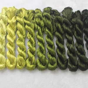 May include: A collection of ten spools of embroidery floss in shades of green, ranging from a light yellow-green to a dark forest green.