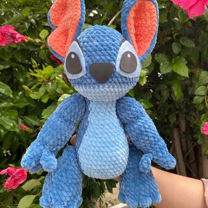 May include: A handmade blue plush toy with large ears, black eyes, and a black nose. The inside of the ears is orange. The plush toy is made of a soft, textured material and is a character from a popular animated film.
