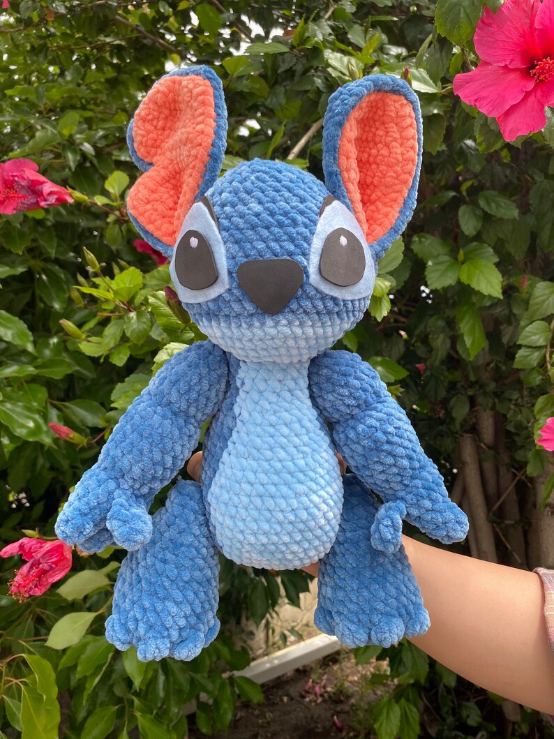May include: A handmade blue plush toy with large ears, black eyes, and a black nose. The inside of the ears is orange. The plush toy is made of a soft, textured material and is a character from a popular animated film.