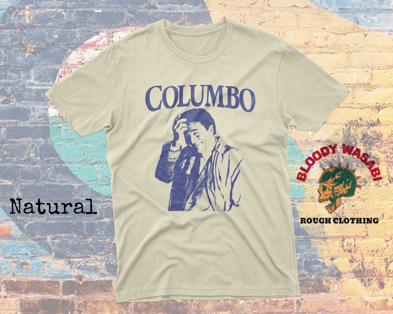 May include: A beige t-shirt with a blue and white graphic print of a man with the text "COLUMBO" above him. The shirt has a small patch on the right sleeve with the text "BLOODY WASABI" and "ROUGH CLOTHING" below it.