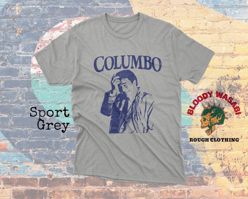 May include: A gray t-shirt with a blue and white image of actor Peter Falk as Columbo, with the text "COLUMBO" above the image. The shirt also features a small logo in the bottom right corner that says "BLOODY WASABI ROUGH CLOTHING".