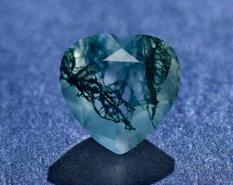May include: A heart-shaped green moss agate gemstone with a clear, translucent center and intricate green moss patterns throughout.