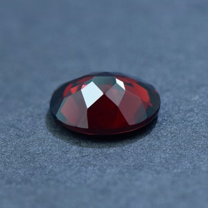 May include: A deep red gemstone with a faceted cut. The gemstone is oval shaped and has a high polish.