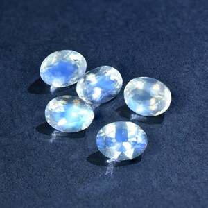 May include: Five oval-shaped moonstone gemstones with a milky white color and iridescent blue flashes.
