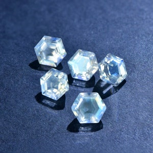 May include: Five iridescent, hexagonal, faceted gemstones in shades of blue and white on a dark blue background.