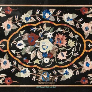 May include: A rectangular black marble tabletop with a floral mosaic design. The mosaic features flowers in shades of white, pink, red, and blue, with green leaves and a gold border. The design is symmetrical and intricate, showcasing detailed craftsmanship.