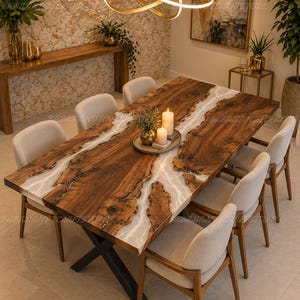 May include: A rectangular dining table featuring a natural wood slab with a live edge and a central translucent white resin river inlay. The table is supported by a black metal X-shaped base and is surrounded by six beige upholstered chairs.