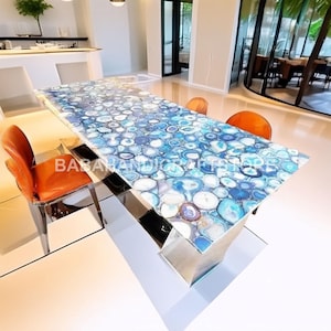 Peut inclure: Une table de salle à manger rectangulaire avec un dessus en pierre d'agate bleue et blanche. La table a une base en métal poli et est entourée de chaises en cuir orange. La surface de la table est faite de nombreuses pierres d'agate circulaires.