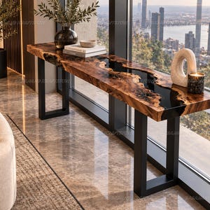 Pode incluir: Uma mesa console longa com uma placa de madeira natural de borda viva e uma incrustação de rio de resina escura e brilhante no centro. A mesa é sustentada por duas pernas de metal preto retangulares e resistentes.