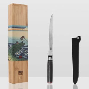 May include: A slender silver-colored knife with a black handle, a black protective sheath, and a tall light-brown wooden storage box. The box features a decorative paper sleeve depicting a stylized ocean wave and a figure, with the brand name KOTAI printed.