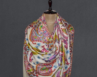May include: A cream-colored scarf with a vibrant paisley pattern in shades of pink, blue, green, and yellow. The scarf is draped over a mannequin, showcasing its intricate design and soft texture. The overall theme is a luxurious and colorful accessory.