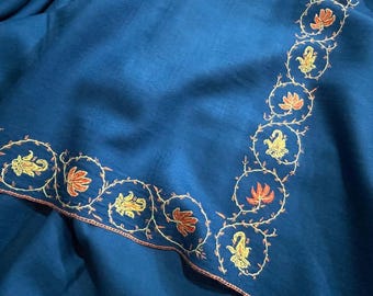 May include: A deep teal textile with an embroidered border. The border features a repeating pattern of gold and orange floral and paisley designs within circular frames, outlined with a thin, reddish-brown thread.