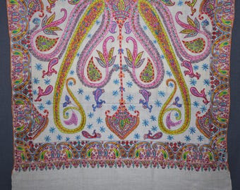 May include: A detailed close-up of a white textile with a colorful paisley pattern. The design features pink, yellow, green, and blue elements, including floral and teardrop shapes. The border has a repeating pattern.