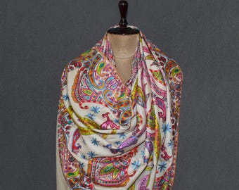 Puede incluir: Un chal blanco con un patrón de paisley en tonos de rosa, azul, verde y amarillo. El chal está drapeado sobre un maniquí.