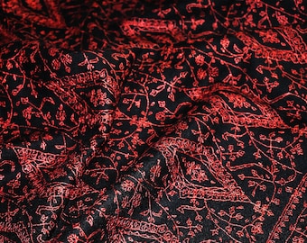 May include: Black fabric with detailed red floral embroidery. The pattern includes delicate vines, leaves, and floral motifs, creating a rich, textured appearance. The fabric is likely a shawl or scarf.