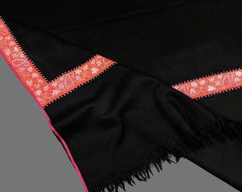 May include: Black shawl with a pink and orange embroidered border. The shawl has a fringe on the bottom edge.