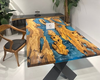 May include: A large wooden dining table with a blue epoxy resin inlay. The table has a black X-shaped base and is shown with a chair.