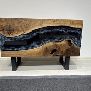 May include: A two-door wooden cabinet with a black resin inlay. The cabinet has a natural wood finish and black metal legs.