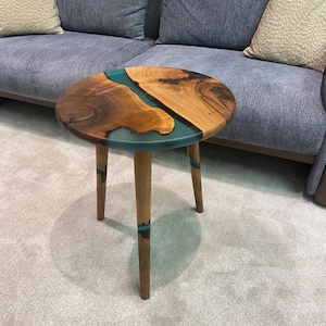 May include: A round wooden side table with a teal blue epoxy resin inlay. The table has three wooden legs.