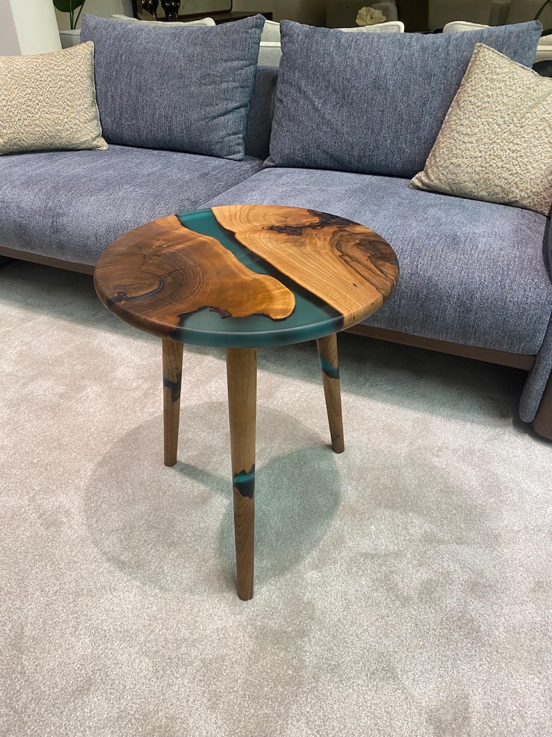 May include: A round wooden side table with a teal blue epoxy resin inlay. The table has three wooden legs.