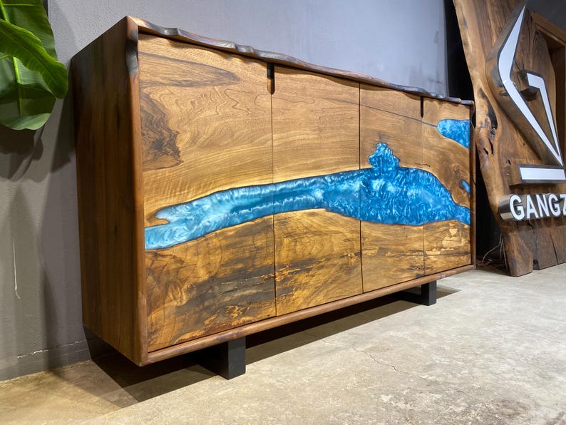 May include: A wooden cabinet with a striking blue resin river design. The cabinet is made of natural wood with a dark finish and features four doors. The blue resin flows across the front, creating a unique and artistic look. The cabinet sits on black legs.