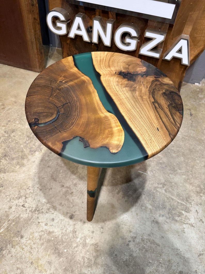 May include: A round wooden table with a teal epoxy river running through the center. The table has a single wooden leg.