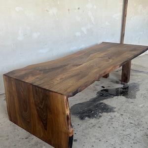 May include: A large, dark brown wooden table with a live edge top and a unique, asymmetrical base. The table is made from a single piece of wood and has a natural, rustic finish.