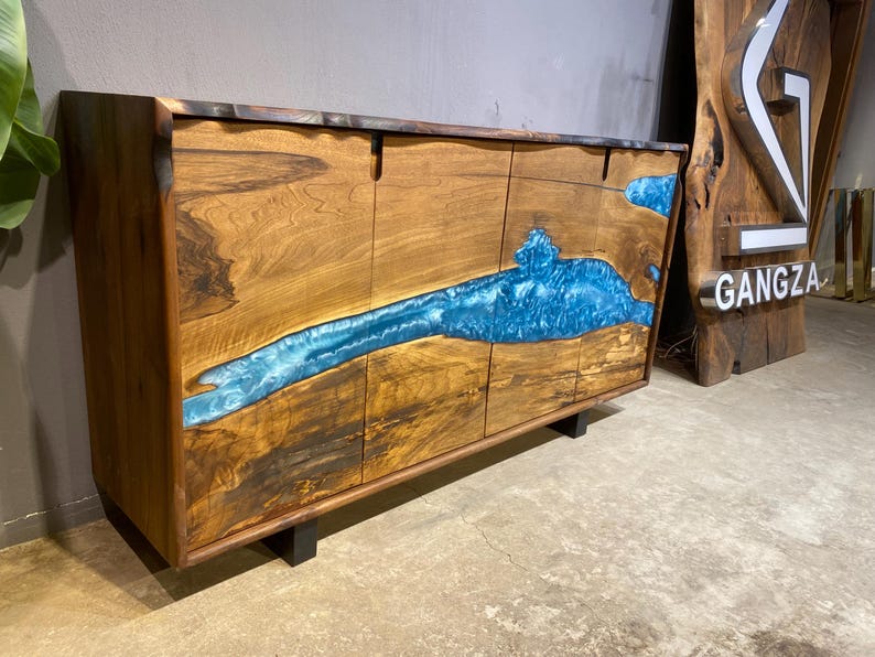 May include: A wooden cabinet with four doors and a striking blue resin river design. The cabinet is made of natural wood with a dark finish and sits on black legs. The word "GANGZA" is visible on a wooden sign.