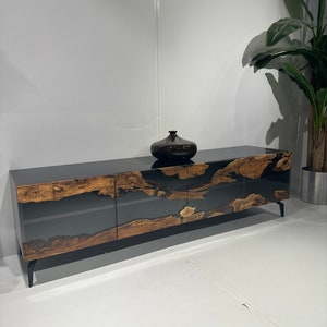 Op de afbeelding: Een lange, zwarte en bruine houten kast met glazen deuren en zwarte metalen poten. De kast heeft een uniek, natuurlijk houtnerfpatroon en is geaccentueerd met zwarte hars.