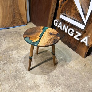 May include: A round wooden side table with a green epoxy resin inlay. The table has three wooden legs.
