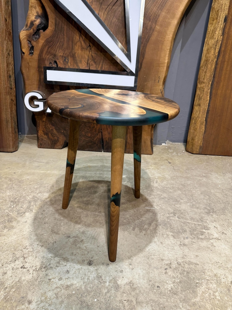 May include: A small round wooden side table with three legs. The table top is made of wood with a blue and black epoxy resin inlay.