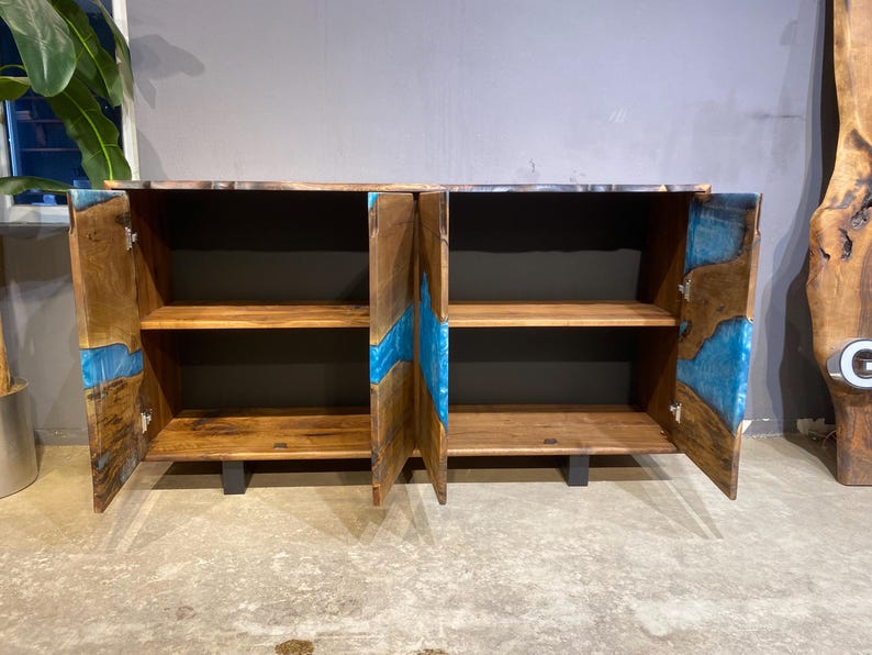 May include: Wooden cabinet with two doors and two shelves. The cabinet is made of brown wood with blue resin accents. The doors are open, revealing the shelves inside. The cabinet is on a gray floor.