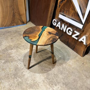 May include: A round wooden side table with a green epoxy resin inlay. The table has three wooden legs.