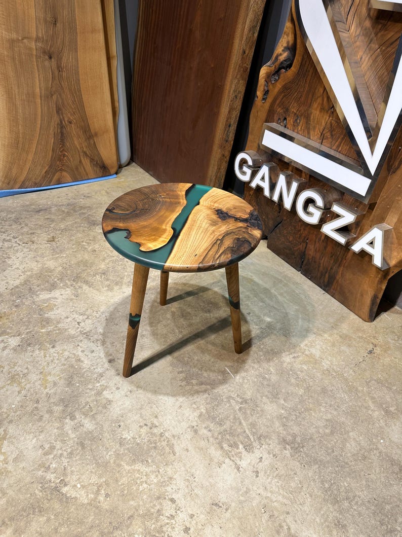 May include: A round wooden side table with a green epoxy resin inlay. The table has three wooden legs.