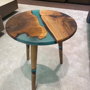 May include: Round wooden side table with a turquoise resin inlay. The table has three wooden legs.