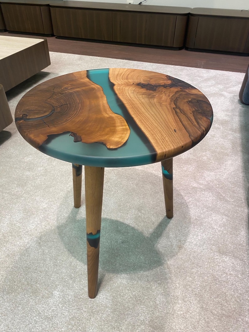 May include: Round wooden side table with a turquoise resin inlay. The table has three wooden legs.