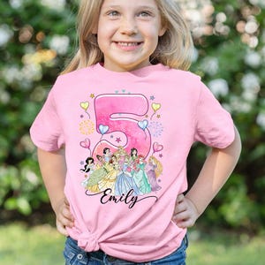A young girl wearing a pink t-shirt with a Disney princess design and the number 5, smiling at the camera.