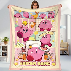 May include: A pink and yellow fleece blanket with a cartoon character design. The blanket features a pink character with different expressions and poses. The text "CUSTOM NAME" is printed on the blanket.