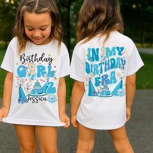 A young girl wearing a white t-shirt with a birthday theme, featuring illustrations of characters from the movie Frozen and the text "In my birthday era" on the back.