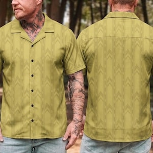 May include: A short-sleeved button-down shirt in a muted olive green color featuring a repeating vertical pattern of subtle chevron arrows. The shirt has a classic camp collar, a straight hem, and a row of dark buttons down the front center.