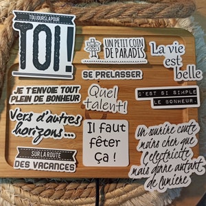 May include: A collection of nine white stickers with black text and illustrations. The stickers feature motivational phrases in French, such as "Toi!" (You!), "Un petit coin de paradis" (A little corner of paradise), "Se prelasser" (To relax), "Quel talent!" (What talent!), "Il faut f&ecirc;ter &ccedil;a!" (We must celebrate this!), "Je t'envoie tout plein de bonheur" (I send you lots of happiness), "Vers d'autres horizons..." (Towards other horizons...), "C'est si simple le bonheur" (It's so simple, happiness), and "Un sourire co&ucirc;te moins cher que l'&eacute;lectricit&eacute; mais donne autant de lumi&egrave;re" (A smile costs less than electricity but gives as much light).
