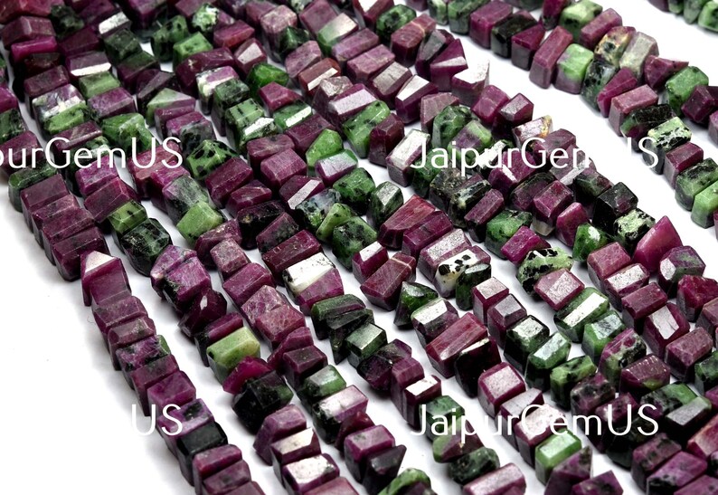 Puede incluir: Hebras de cuentas de rub&iacute; zoisita en bruto. Las cuentas son una mezcla de colores rojo intenso y verde, cortadas en formas rectangulares irregulares. Las cuentas est&aacute;n ensartadas, creando una superficie texturizada.