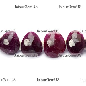 May include: Six faceted, oval-shaped ruby gemstones with a deep red hue are displayed against a white background. The gemstones have multiple facets that catch the light, creating a sparkling effect. The text "JaipurGemUS" is repeated across the top and bottom of the image.